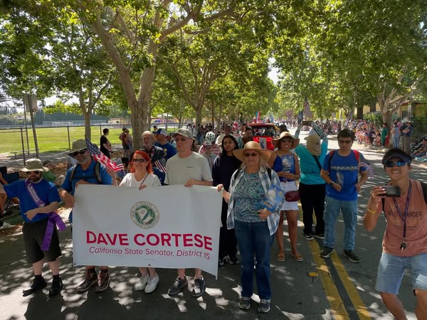 Community volunteers parading with Senator Cortese, holding a banner and flags 