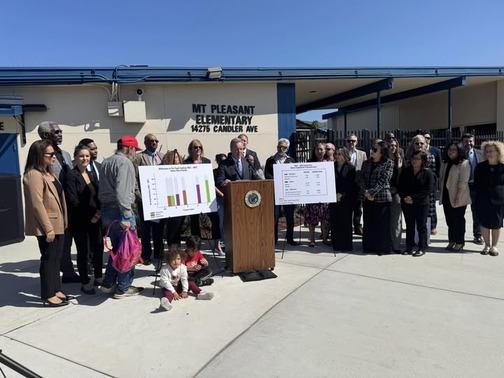 Senator Cortese at a podium outside Mt. Pleasant Elementary School, surrounded by community members and posters.