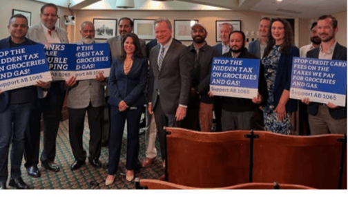 Senator Cortese standing next to Assemblymember Liz Ortega for a photograph, surrounded with community members holding signs that read “Stop the hidden tax on groceries and gas! Support AB 1065” and “Stop credit card fees on the taxes we pay for groceries and gas. Support AB 1065.”