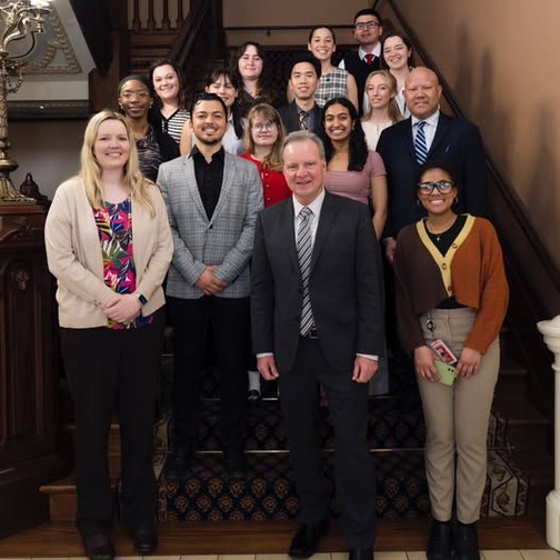 Senator Cortese at the bottom of a carpeted staircase, surrounded by Capitol Senate Fellows, all smiling for a photograph.