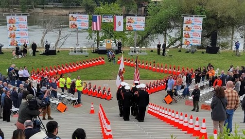 A birds-eye view of the #Caltrans Fallen Workers Memorial. Soldiers hold flags, surrounded by bright orange cones arranged in a diamond shape. 