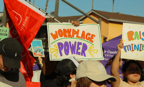 Poster from the 2024 May Day Rally, held up by a hand, reading “workplace power”