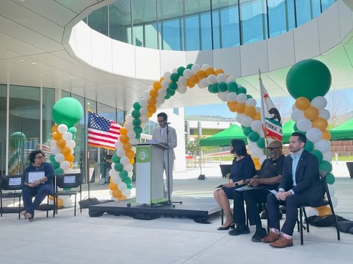 Evergreen Valley College leadership speaking at a podium, surrounded by other leadership and celebratory green, white, and yellow balloons.
