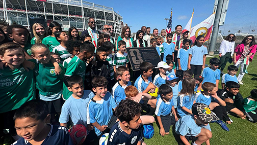 A crowd of young athletes, photographed in soccer gear around a commemorative plaque.