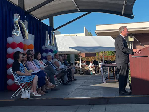 Senator Dave Cortese at a podium on stage, speaking to graduates.